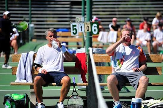 Water bottle and towel on a shaded court-side bench during a rest block between ball machine drills