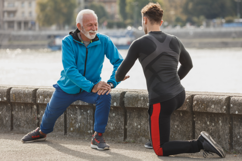 Two players doing a supported lunge and hip stretch outdoors before training — mobility work that prepares the hips for tennis movement