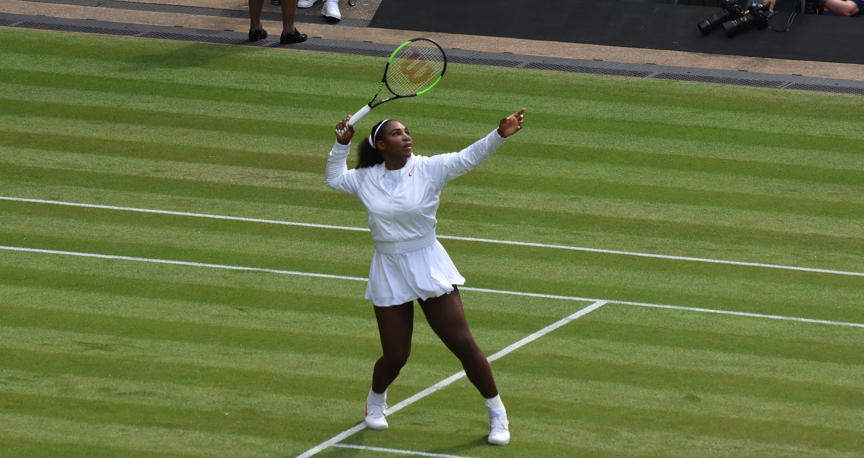 Player turned sideways under a lob with the non-hitting arm raised, preparing an overhead during ball machine practice
