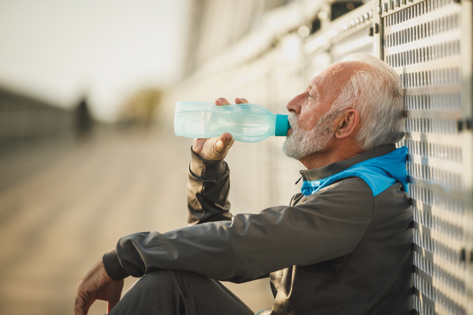 A player sitting against a fence taking a water break between training blocks — planned rest is part of arm-friendly ball machine practice