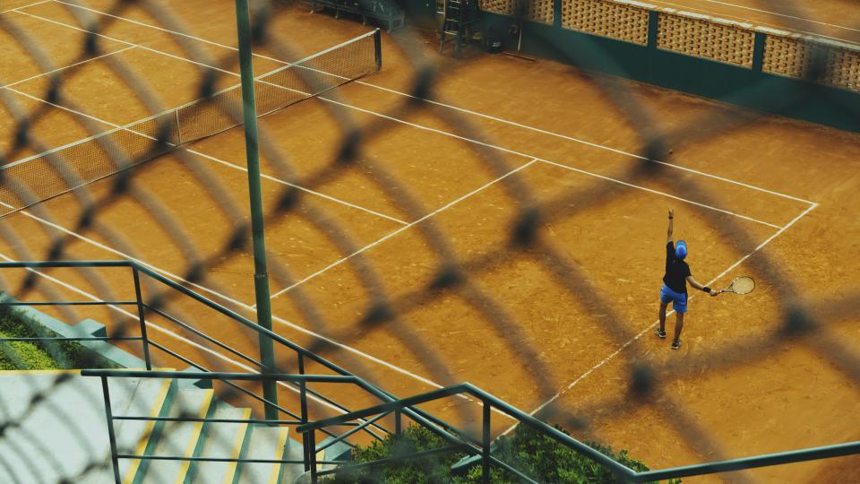 Elevated view of a singles player alone on a full-size court, showing the court space a singles tennis pattern has to cover
